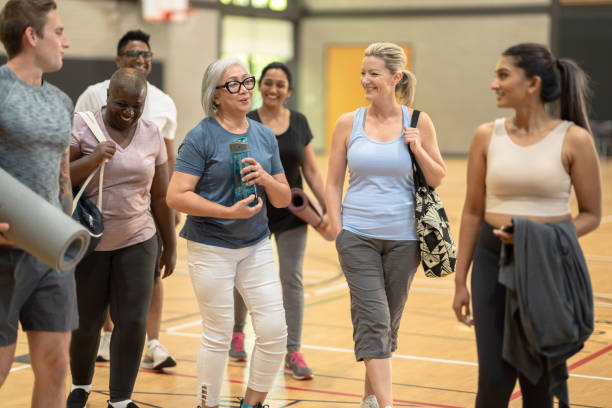 Fitness class goers get to know each other A diverse group of adults walk out of a gymnasium after a fitness class smile as they talk to each other. community health center stock pictures, royalty-free photos & images