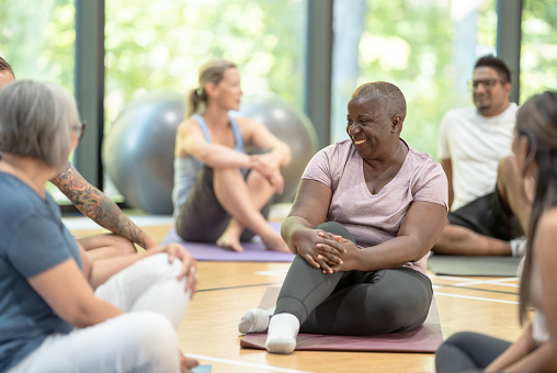 A diverse group of adults sit on their yoga mats and chat happily with each other.