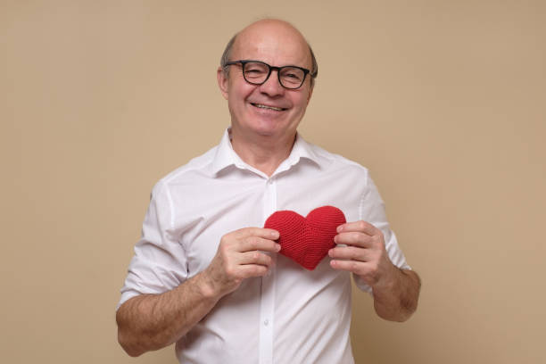 Senior gentleman in glasses holding a red heart smiling. stock photo