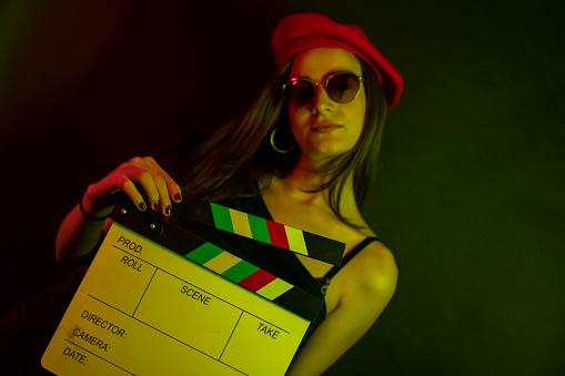 Photo of gorgeous woman 20s smiling and holding clapperboard.High Fashion model woman in colorful bright neon blue and purple lights