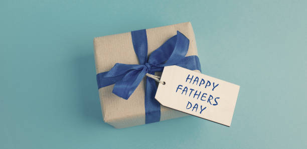 istock Small gift box with a ribbon on a blue colored background, happy fathers day present 1361401129