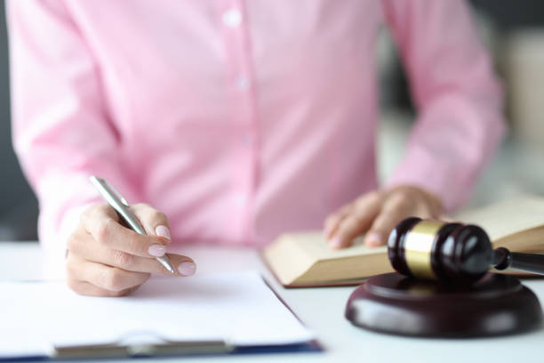 Woman judge writing in documents with ballpoint pen near hammer of courthouse stock photo