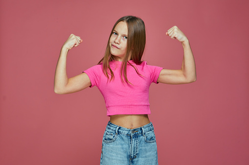 Poderosa niña deportiva muestra músculos bíceps, levantando las manos sobre fondo rosa de estudio. Concepto de reglas para niñas photo