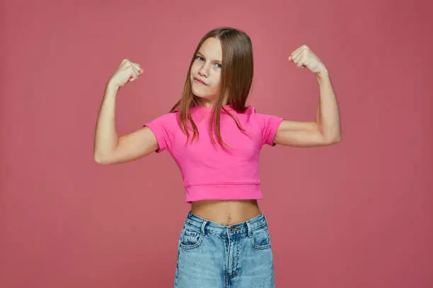 Photo of Powerful sporty child girl show biceps muscles, raising hands on pink studio background. Girls rules concept
