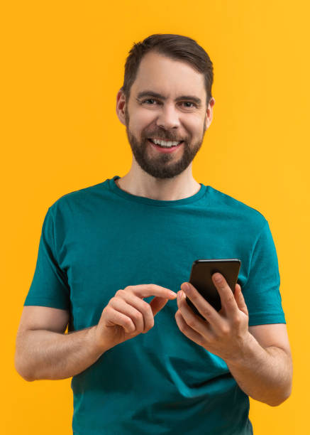 istock Vertical image of young smiling bearded man holding smartphone in hands and making bets online at bookmaker's website using mobile application 1361404455