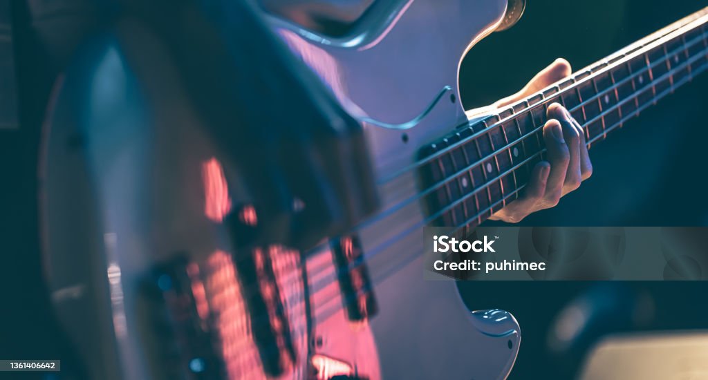 Close-up of a man playing the bass guitar. Close-up of a man playing bass guitar at a concert in the dark. Bass Guitar Stock Photo