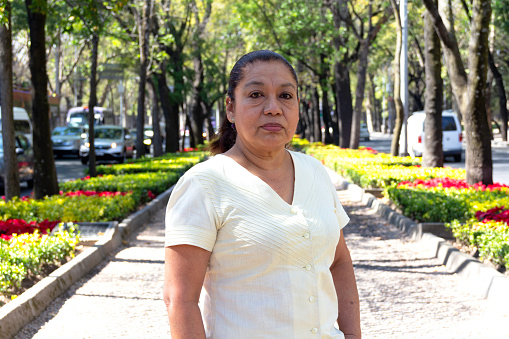 Mature Mexican lady looking in front of the camera, standing, between city streets. Latin woman looking at the camera. serious attitude.