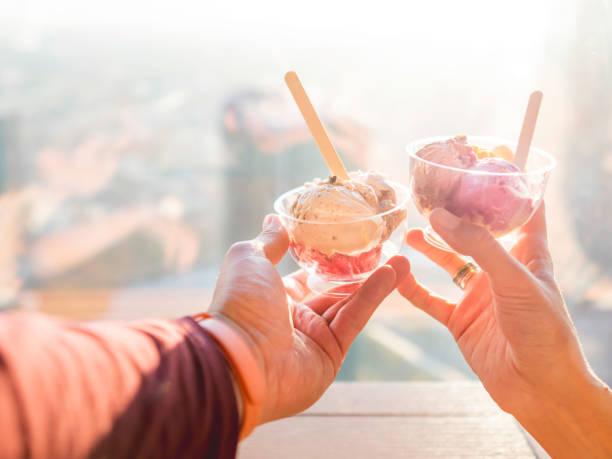 Man and woman holds plastic bowls with colorful balls of ice-cream. Cold dessert for sunny days. Different gelato with wooden spoons. Romantic date in cafe. stock photo