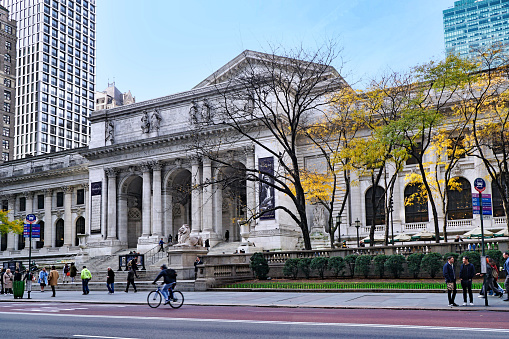 New York City, USA - November 17, 2021:  People walk on the sidewalk in front of the main branch of the New York Public Library on Fifth Avenue.