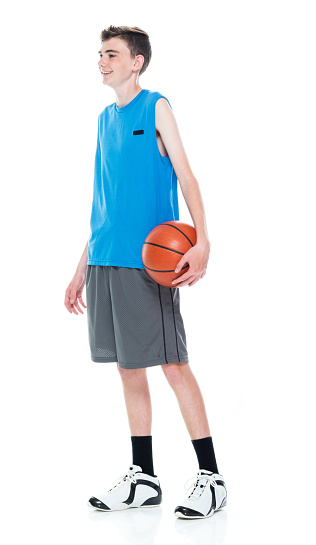 Profile view of aged 12-13 years old caucasian teenage boys basketball player standing in front of white background and holding basketball - ball and using sports ball