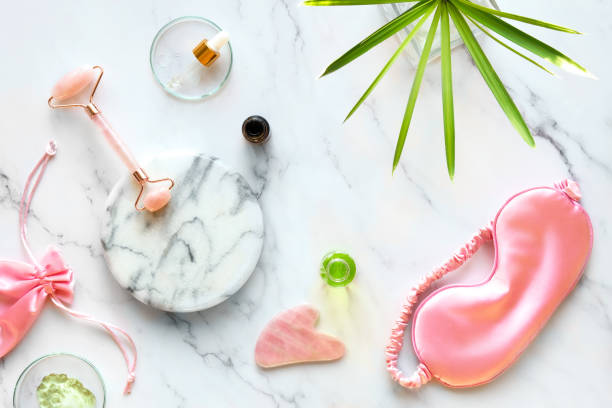 istock Facial massage. Moisturizer, pink rosa quarz face roller and gua sha stone on marble surface. Green plant leaf is Cylindric Sedge 1361413832