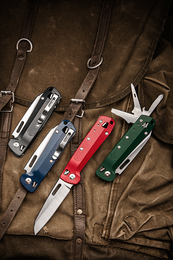 Folding multitool penknives on a khaki canvas backpack. A pocket-sized tool for hiking and daily life.