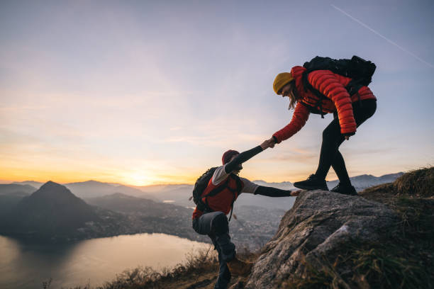 Hiking couple climb up mountain ridge Young woman offers man a hand up, in the Swiss Alps hiking stock pictures, royalty-free photos & images