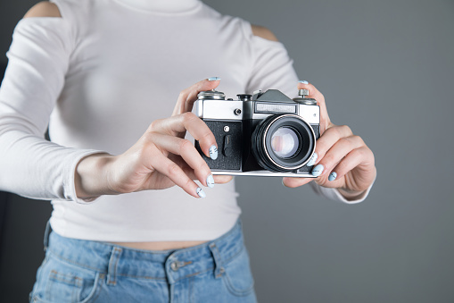 young woman holding an old camera on a gray background