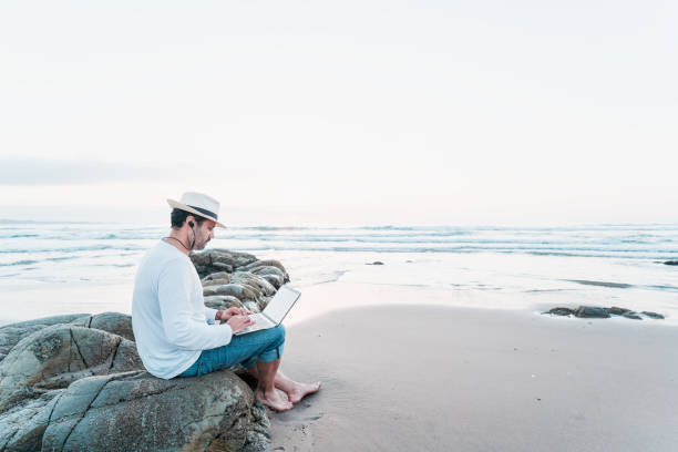 istock man sitting on the beach with a laptop alone doing telecommuting or remote work 1361435810