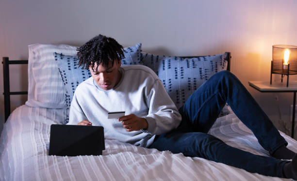 Young African-American man on bed shopping online
