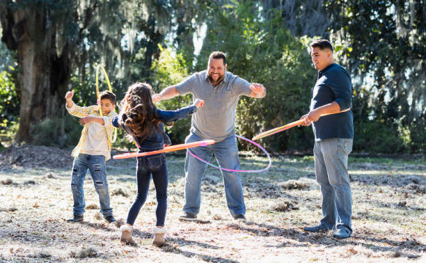 padres e hijos hispanos en el parque jugando con aros - hooping fotografías e imágenes de stock