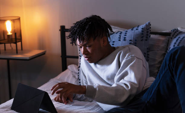 istock Young African-American man on bed using digital tablet 1361443509