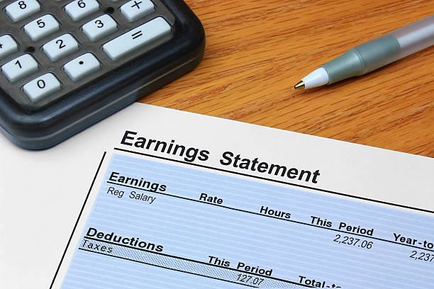Earnings Statement An itemized earnings statement showing earnings and deductions, on a desk with a calculator and pen. paycheck photos stock pictures, royalty-free photos & images