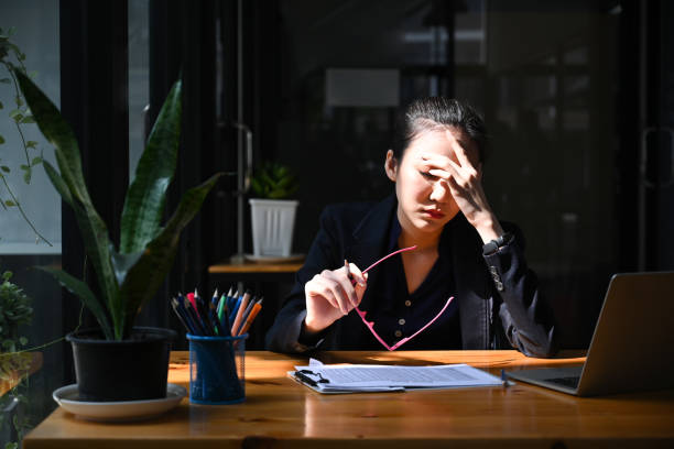 una donna d'affari oberata di lavoro si toglie gli occhiali e si massaggia la testa. - frustrazione foto e immagini stock