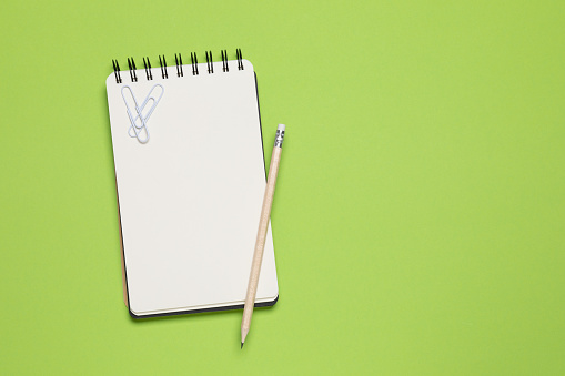 Spiral notebook and pencil isolated on green background