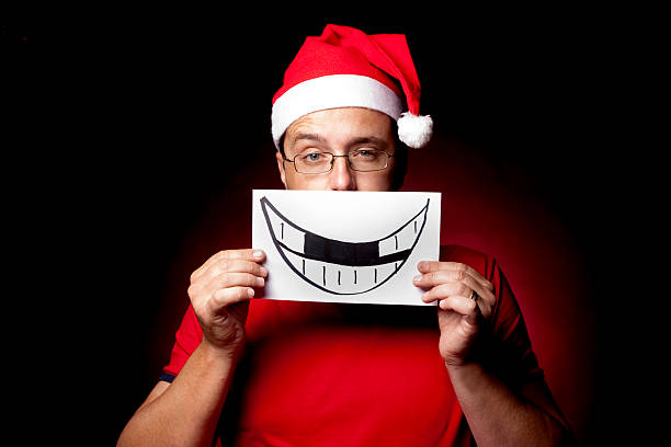Man in Santa Hat holding up a drawing of a child's smile to his face, with his eyebrow arched.