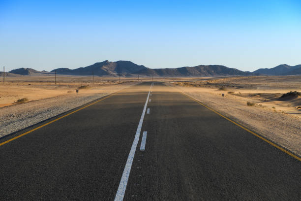 istock Red sand blowing over Namib desert road wide 1361457790