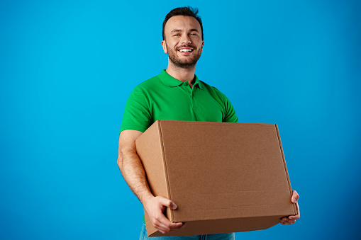Delivery man with box in photo studio against blue background