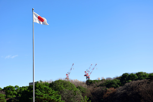 Japanese flag swaying in the wind in front of the forest and crane against clear sky.