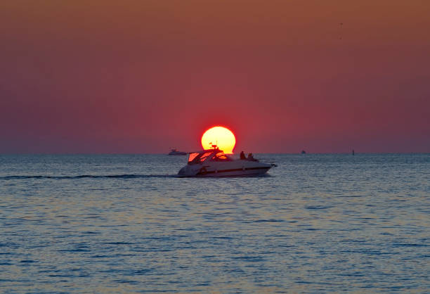 A motor boat on the water near the solar disk against the background of a ruby sky. Sochi, Russia, 2021