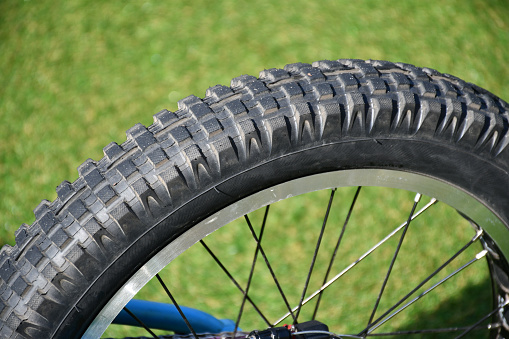 part of a wheel made of gray black rubber tire and metal spokes on a bike in the street