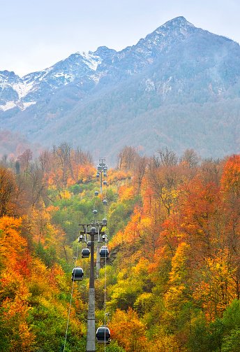 Cabbies of the cable car among autumn trees on the background of the mountain peak of the Caucasus. Rosa Khutor, Sochi, Russia, 2021