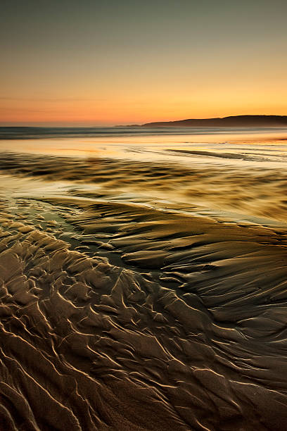 long exposure a wave washing up onto a sandy beach at dawn