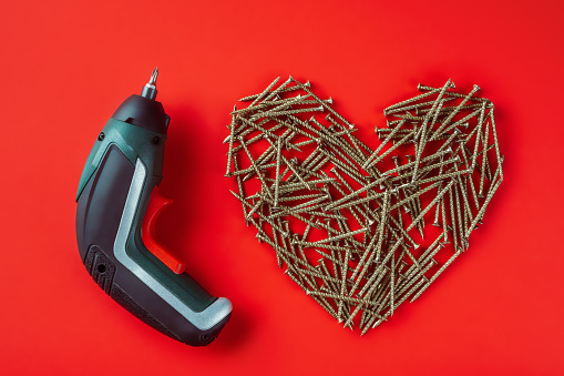 Long metal screws laid out randomly in shape of heart and stud driving machine on red background. Heart relation concept. Construction concept. Flat lay. Copy space. Mock up