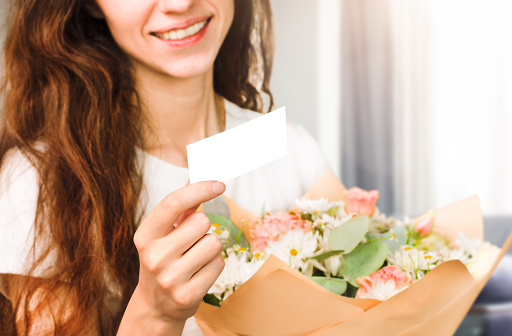 happy young woman holding a bouquet of flowers and a note