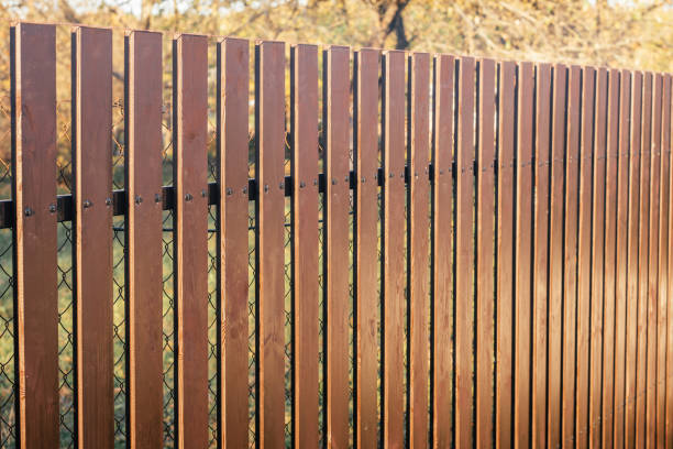 new modern wooden brown fence on chain-link fence background around yellow trees close up new modern wooden brown fence with black tacks on chain-link fence background around yellow trees in autumn outdoor in sunny day close up. High quality photo wood and wire fence designs pictures stock pictures, royalty-free photos & images