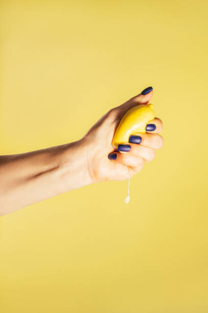 Female hand with blue nails hold fresh lemon isolated on yellow. Squeeze out juice. Finger crush. Vertical, copy space stock photo