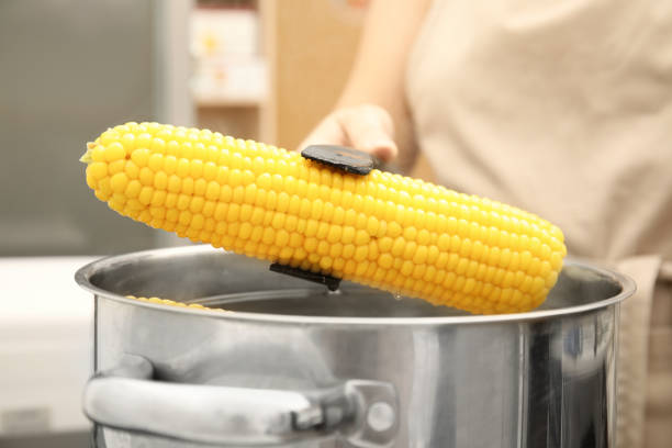 Woman taking boiled corn from pot with tongs in kitchen, closeup