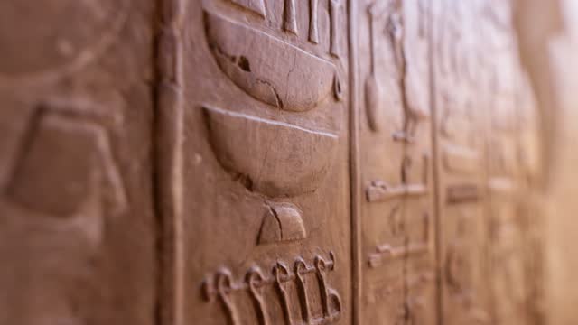 Close shot of Egyptian hieroglyphs on the wall in Hatshepsut temple. Antique stone wall with carved ancient Egyptian hieroglyphs. Shallow DOF