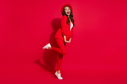 Full length profile photo of cool brunette lady look empty space wear cap suit shoes isolated on red color background.