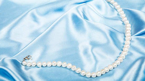 pearl beads on light blue luxury satin fabric. Background. elegant wallpaper. Selective focus