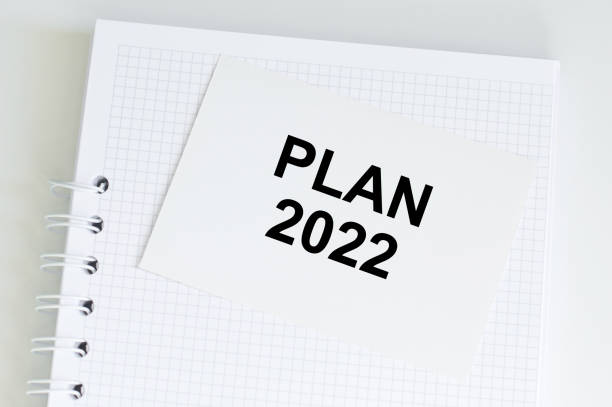 istock Plan 2022 inscription on a card that sits on a white blank notebook on the table 1361486321
