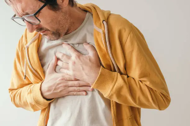 Photo of Aching chest, adult male with painful grimace pressing the upper abdomen with his hands to ease pain