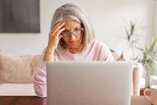 istock Sad middle-aged woman sit at table in living room using laptop 1361489669