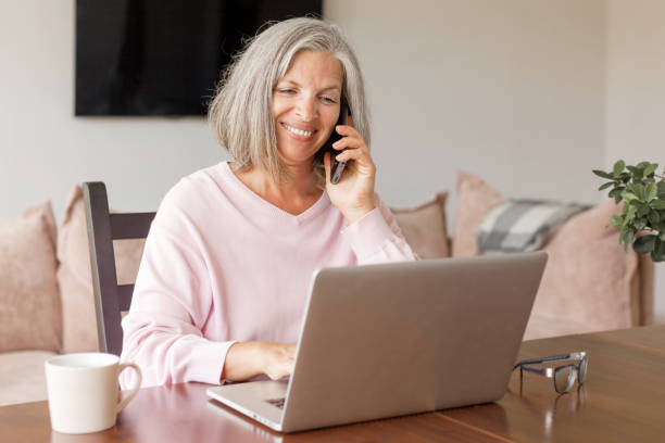 istock Happy middle age senior woman sitting at the table at home working using computer laptop 1361489672