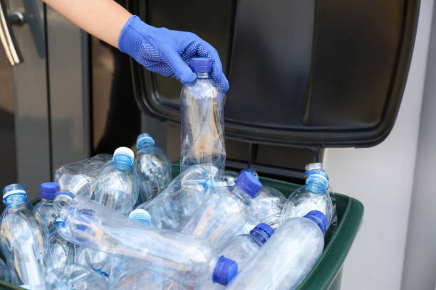 istock Woman in gloves putting used plastic bottle into trash bin outdoors, closeup. Recycling problem 1361492978