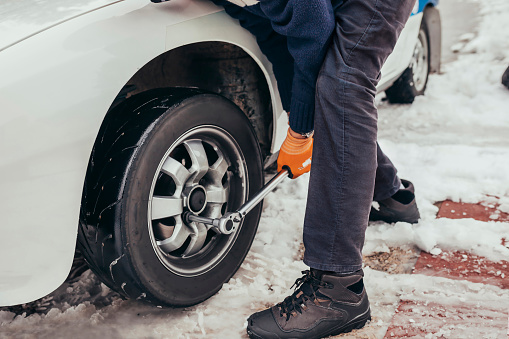 Senior pilot wearing orange gloves and winter clothes, changing car wheel on a classic car before a race. Mechanic working with old automobile.