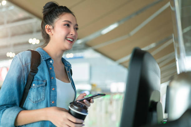 smart asian female traveller self checking in for flight transport at gate counter machine scaning monitor device at airport check in counter,smart technology travel ideas concept at terminal stock photo