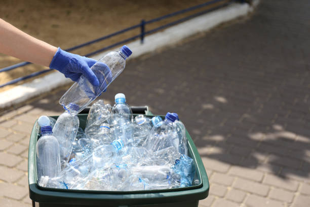 istock Woman in gloves putting used plastic bottle into trash bin outdoors, closeup. Recycling problem 1361493871