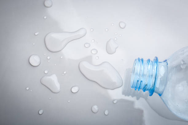 Drops of spilled water and plastic bottle on grey background, top view